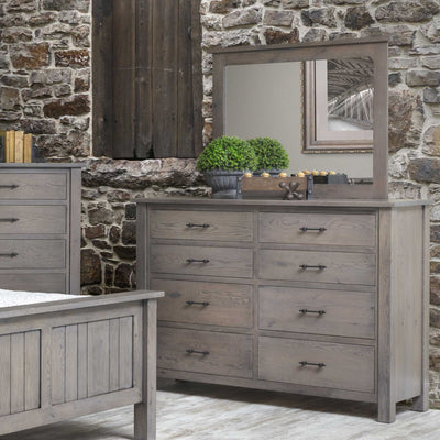 Weathered gray oak eight-drawer dresser with matching wood-framed mirror styled against a rustic stone wall