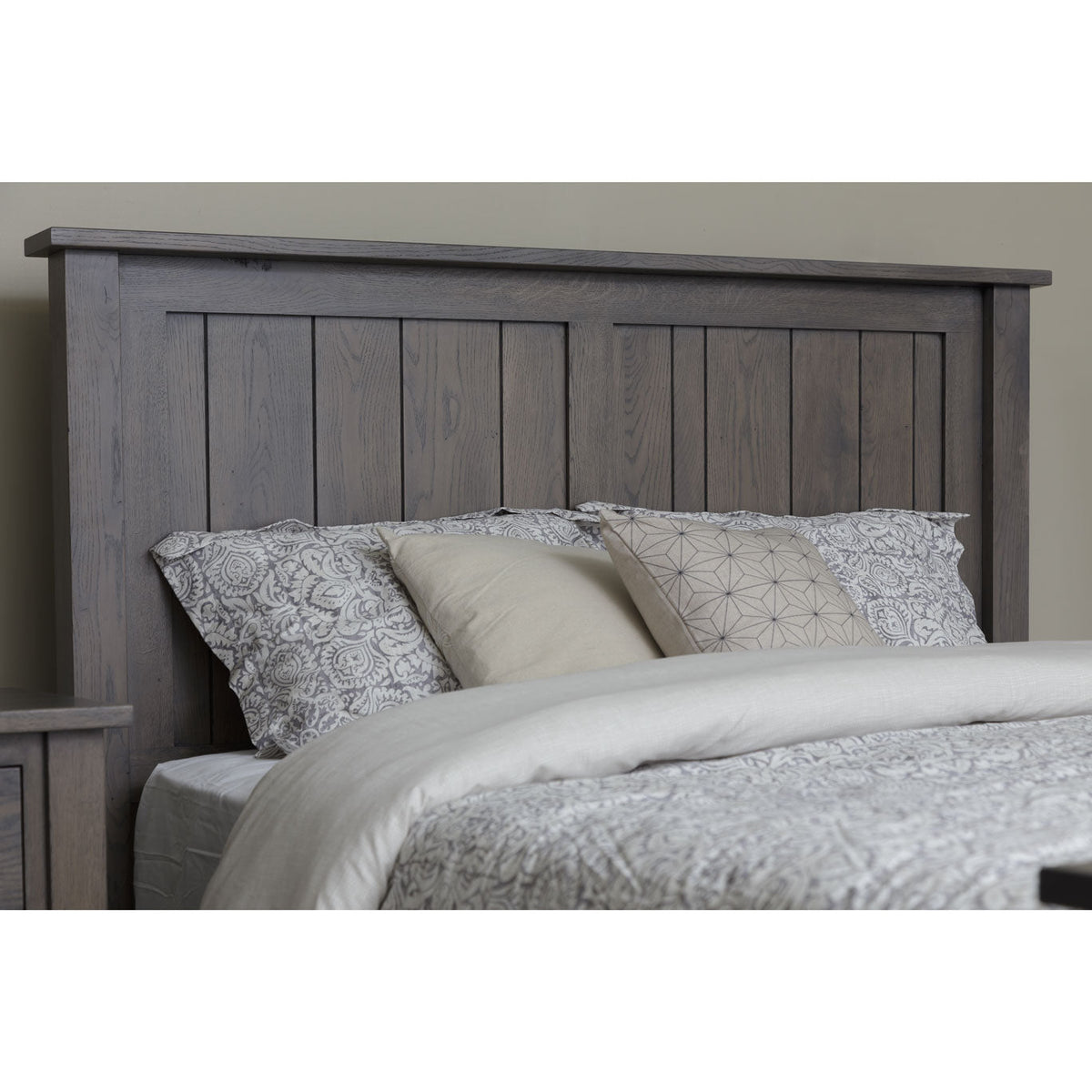 Gray oak plank headboard with a beveled top cap above floral and linen pillows in a neutral bedroom