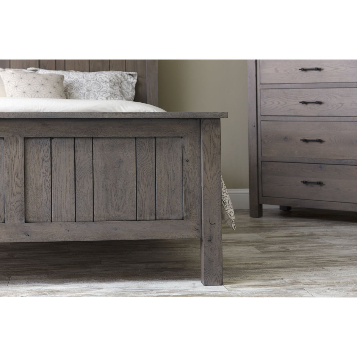 Angled view of the gray panel bed footboard and square leg with a matching chest of drawers in the background