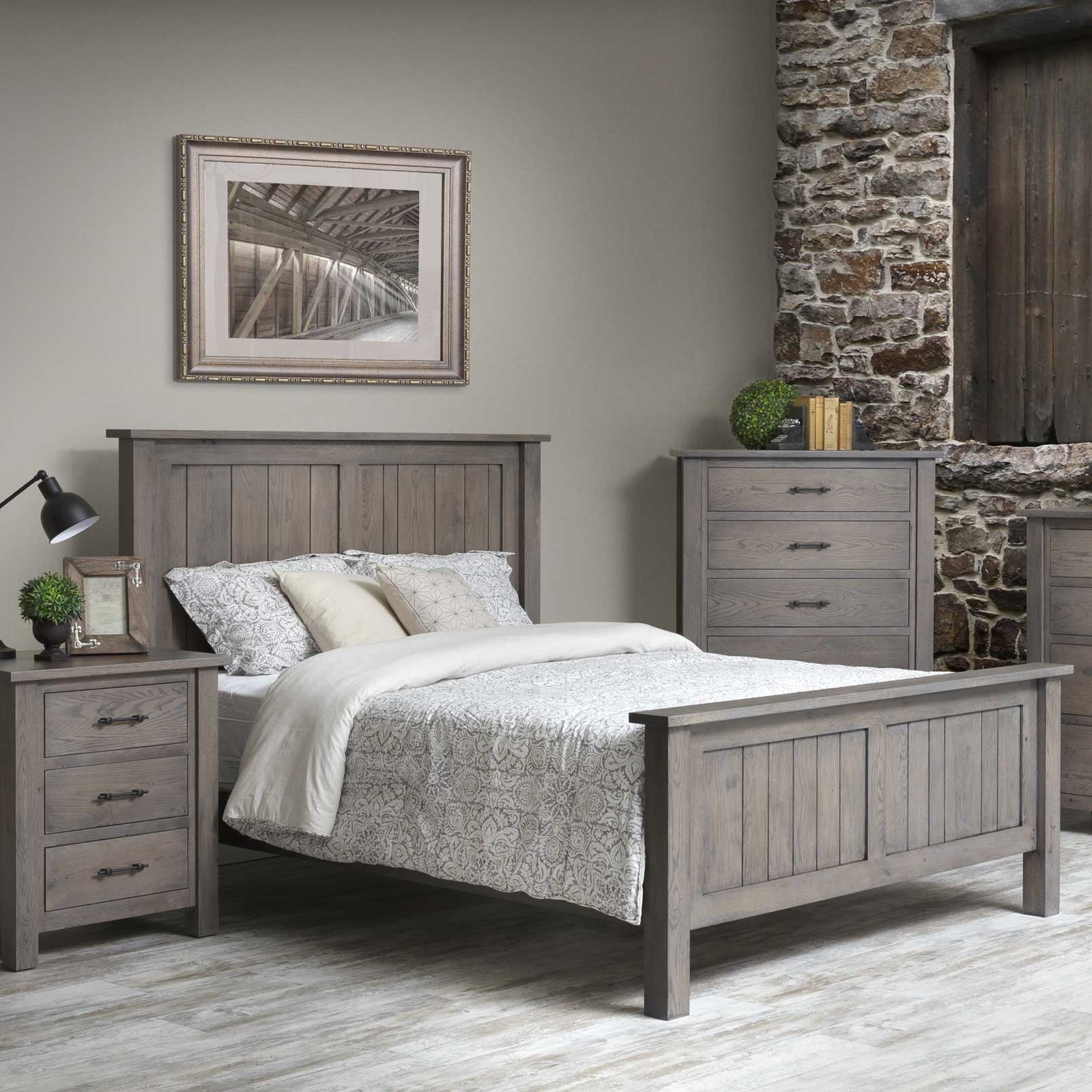 Gray plank panel bed dressed in floral bedding between a three drawer nightstand and a tall chest of drawers