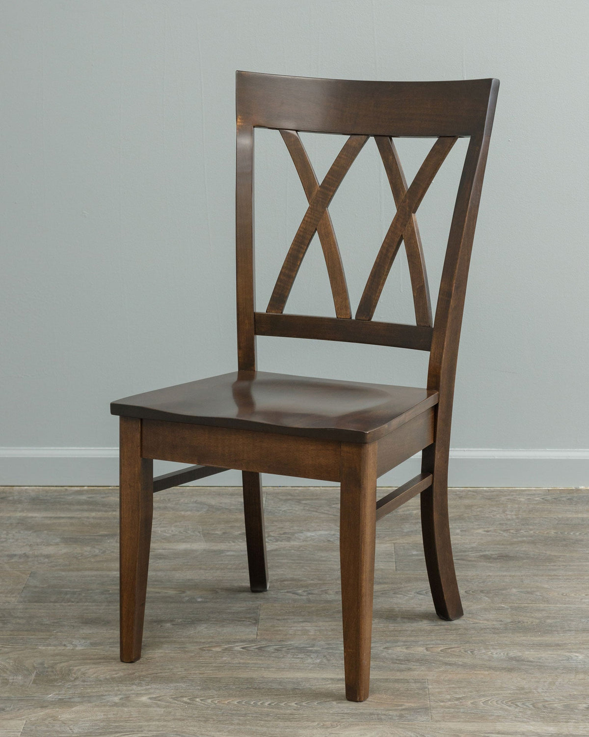 Dark brown double X back dining chair photographed at an angle against a gray wall and wood plank floor