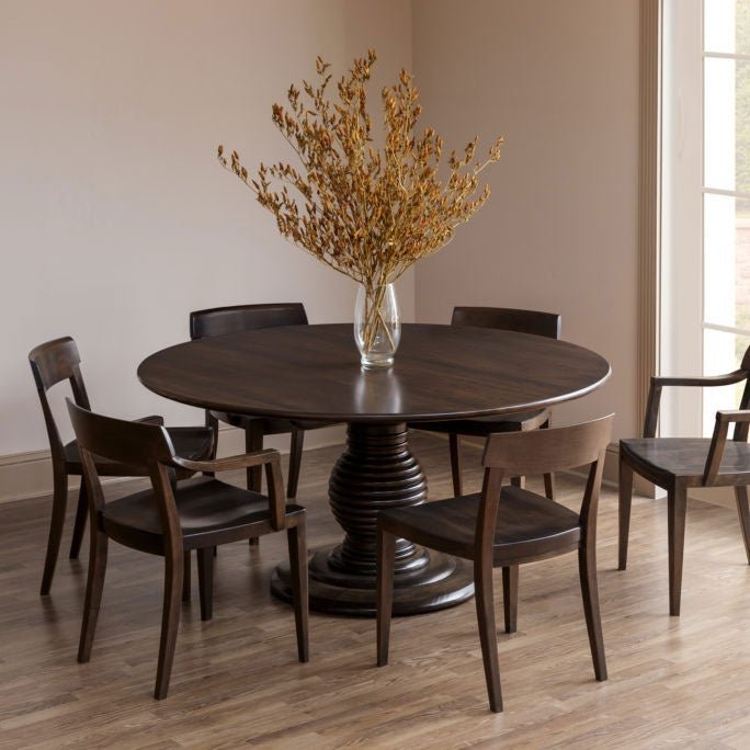 Round pedestal dining table in dark walnut with a beehive turned base, six curved back chairs and a dried floral vase