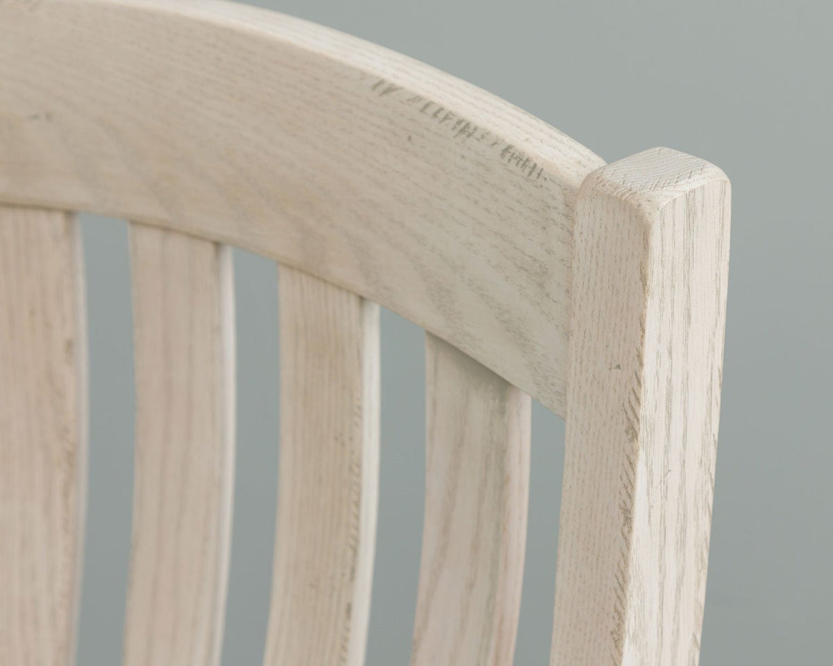 Detail of the whitewashed chair's rounded top rail corner and slats against a soft gray background