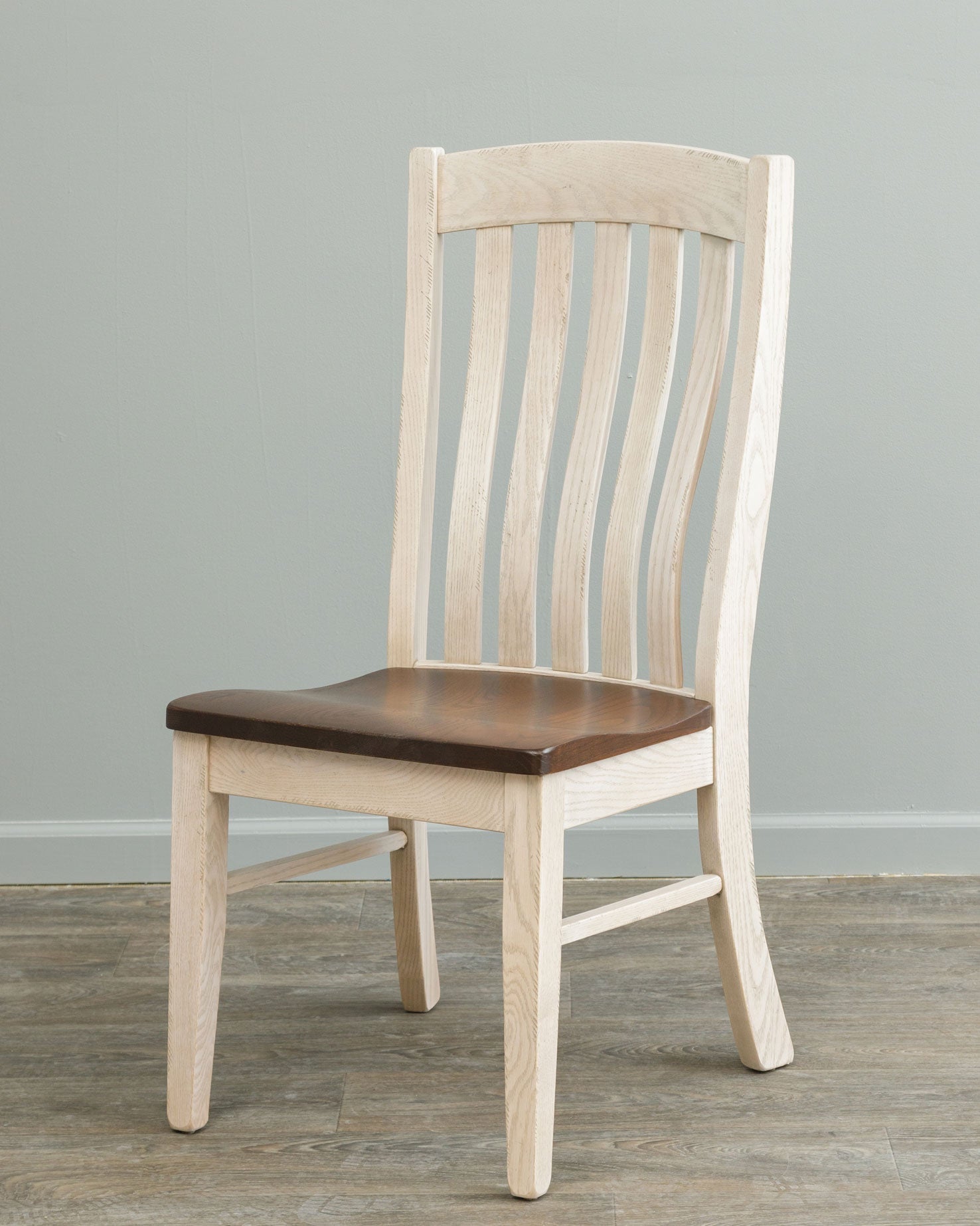 Sage green painted slat back dining chairs with stained wood seats around a two-tone pedestal dining table