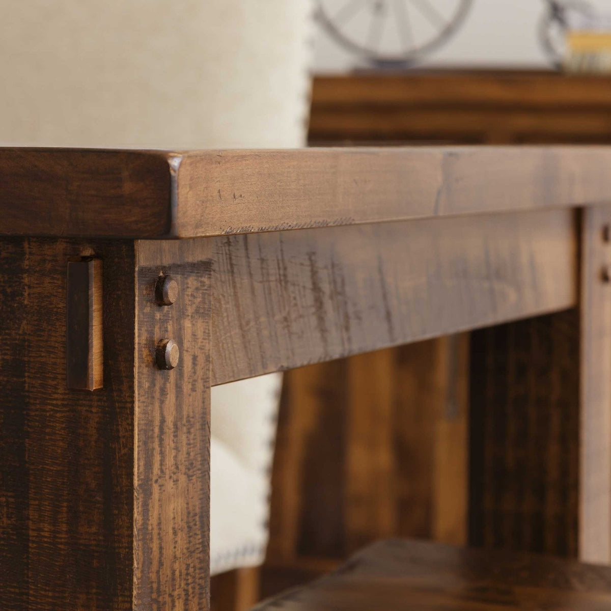 Close-up of the rustic table's beveled plank top edge, pegged apron joinery and heavy square leg