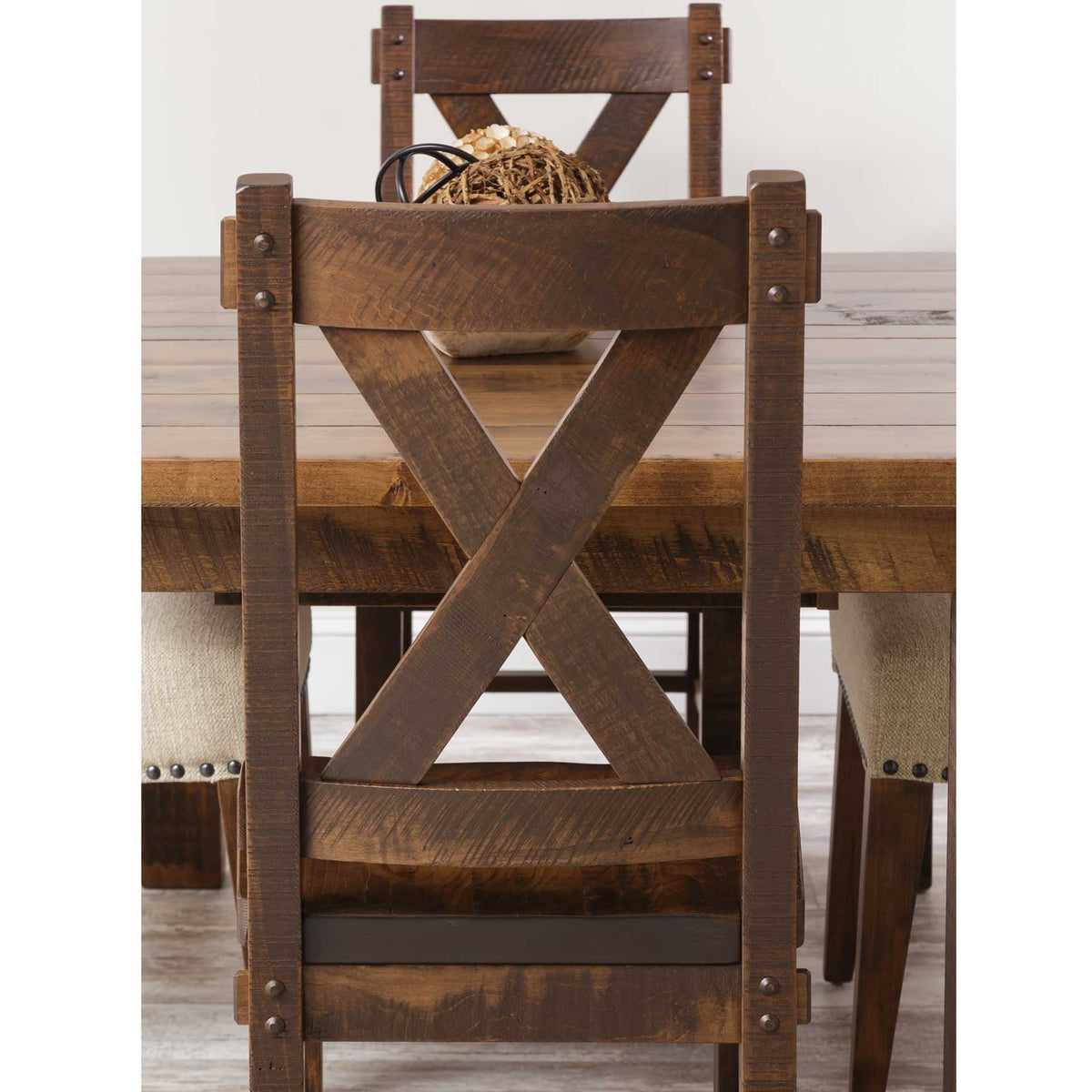 Back view of a rustic X back dining chair with iron rivet accents beside the plank dining table