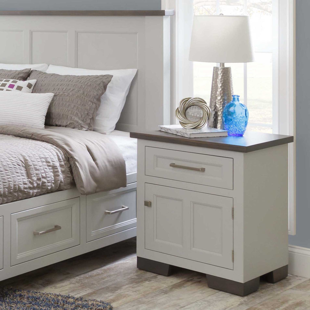 White nightstand with gray wood top styled beside a matching white storage bed with under-bed drawers in a bright bedroom