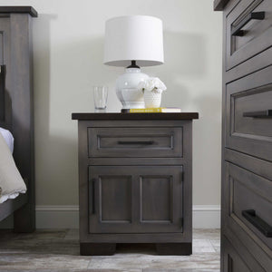 Gray solid wood nightstand with one drawer and a two-panel door, dark rustic top, styled with a white lamp between bed and dresser