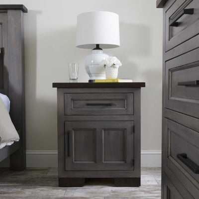 Gray solid wood nightstand with one drawer and a two-panel door, dark rustic top, styled with a white lamp between bed and dresser