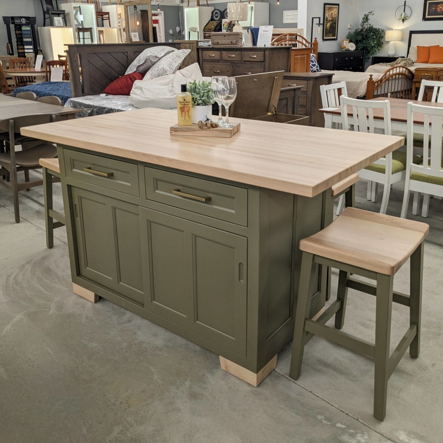 Olive green kitchen island with thick maple butcher block top, brass pulls, sliding doors and saddle bar stools in the showroom