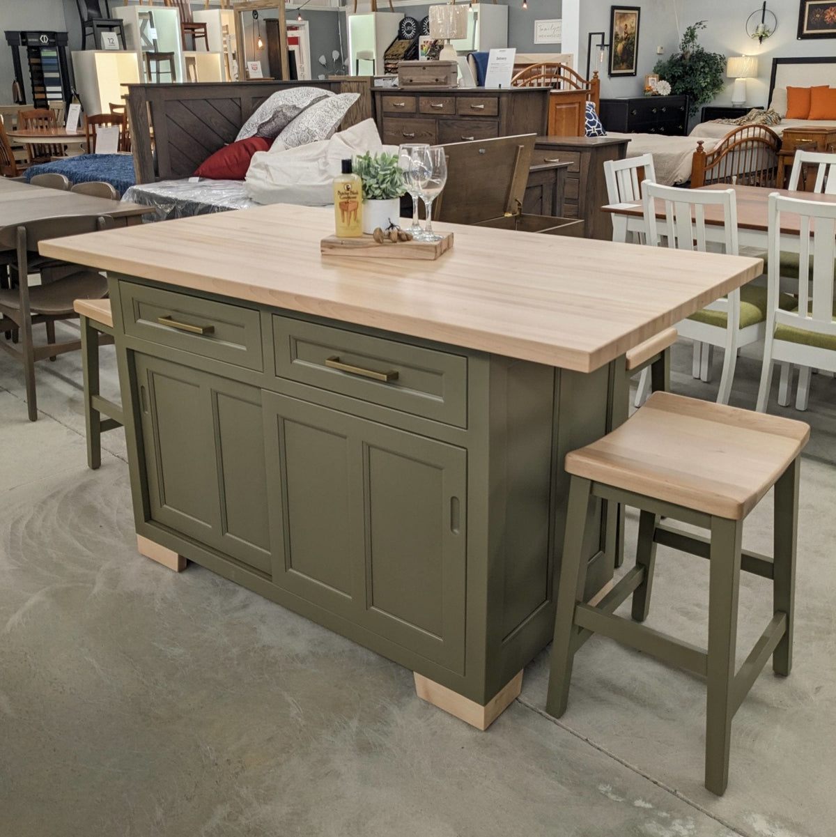 Olive green kitchen island with thick maple butcher block top, brass pulls, sliding doors and saddle bar stools in the showroom