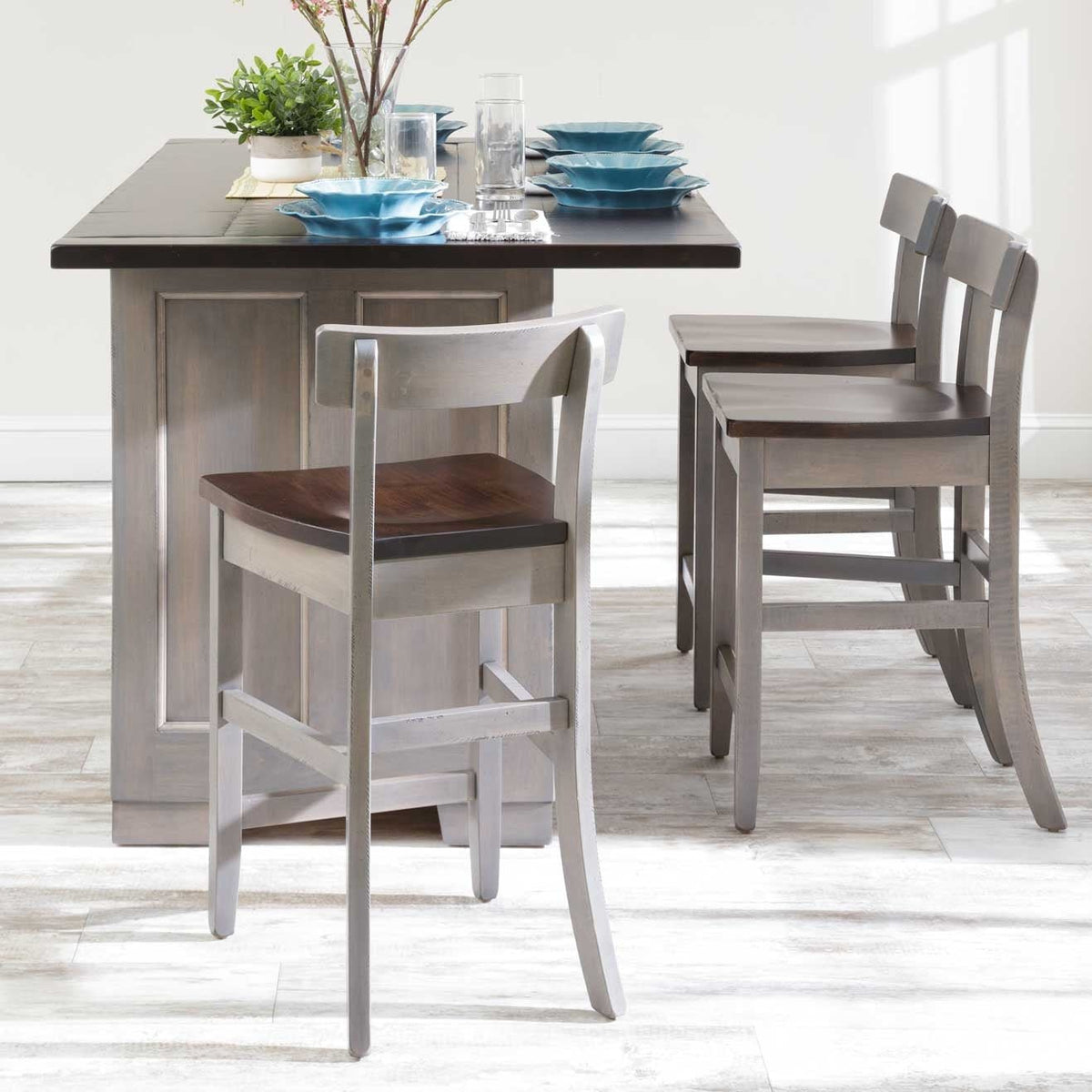 Gray kitchen island set for dining with blue dishes and three two-tone counter-height stools with low backs