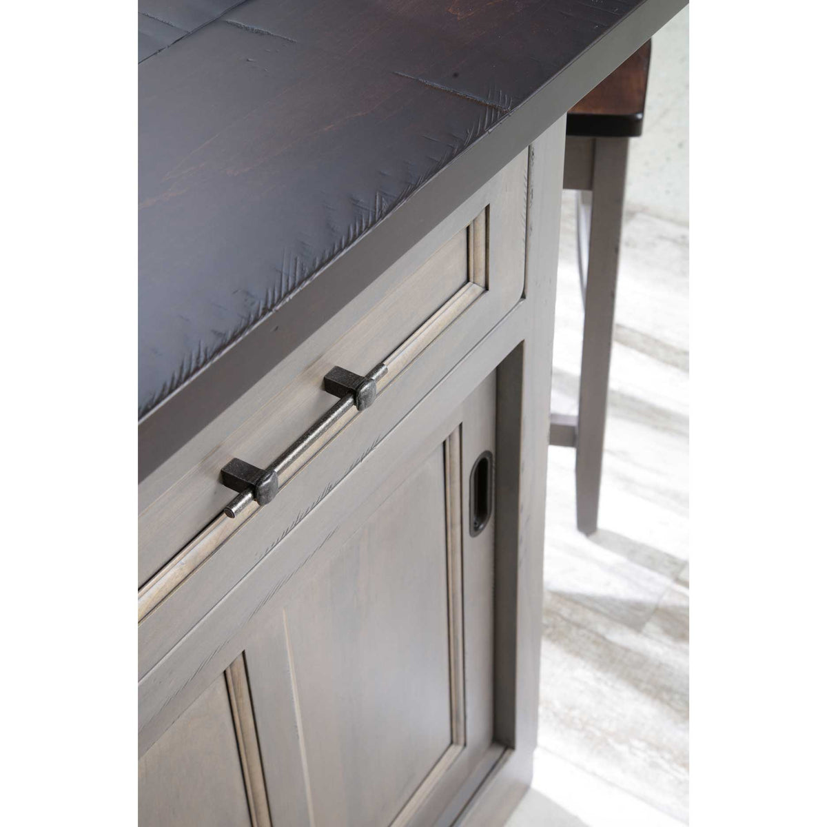 Close-up of the island's rough-sawn dark brown top edge, hand-forged iron drawer pull and sliding door track