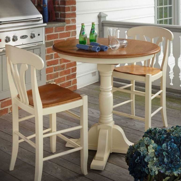 Cherry topped round pub table with painted base and two counter stools styled on a porch beside a brick grill island