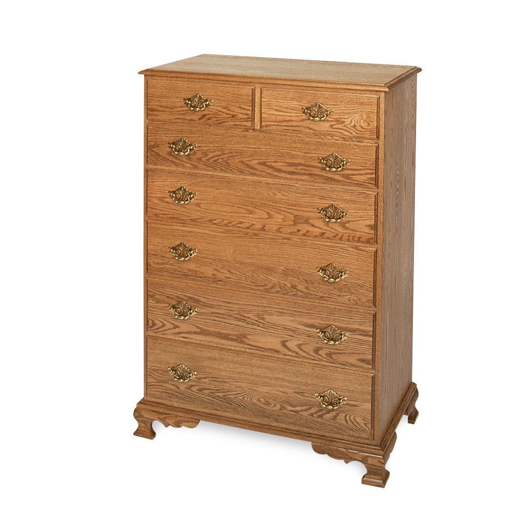 Golden oak chest of drawers shown at an angle with seven graduated drawers and decorative brass batwing pulls