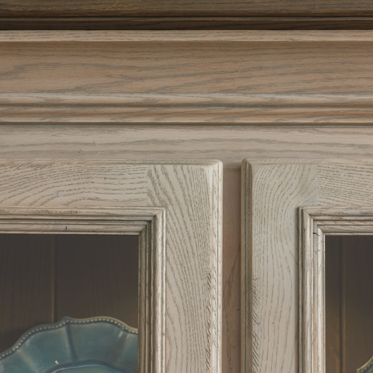 Close-up of the white oak hutch crown molding and beveled glass door frames above blue dishes