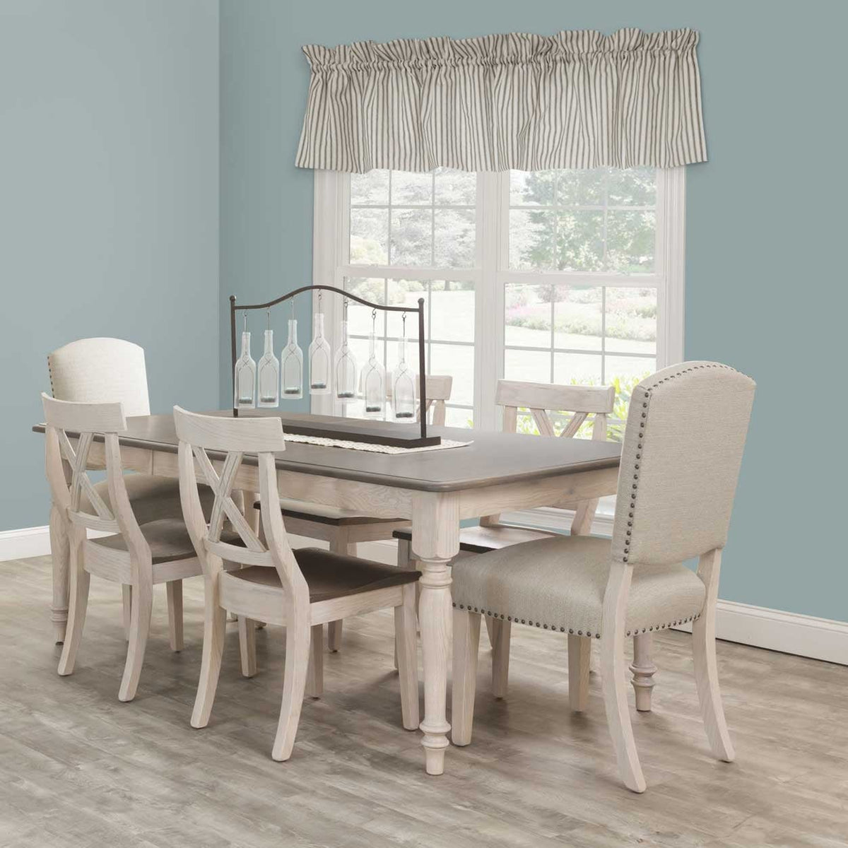 Whitewashed farmhouse dining table with a gray-stained top, shown with X-back wood chairs and cream upholstered nailhead dining chairs