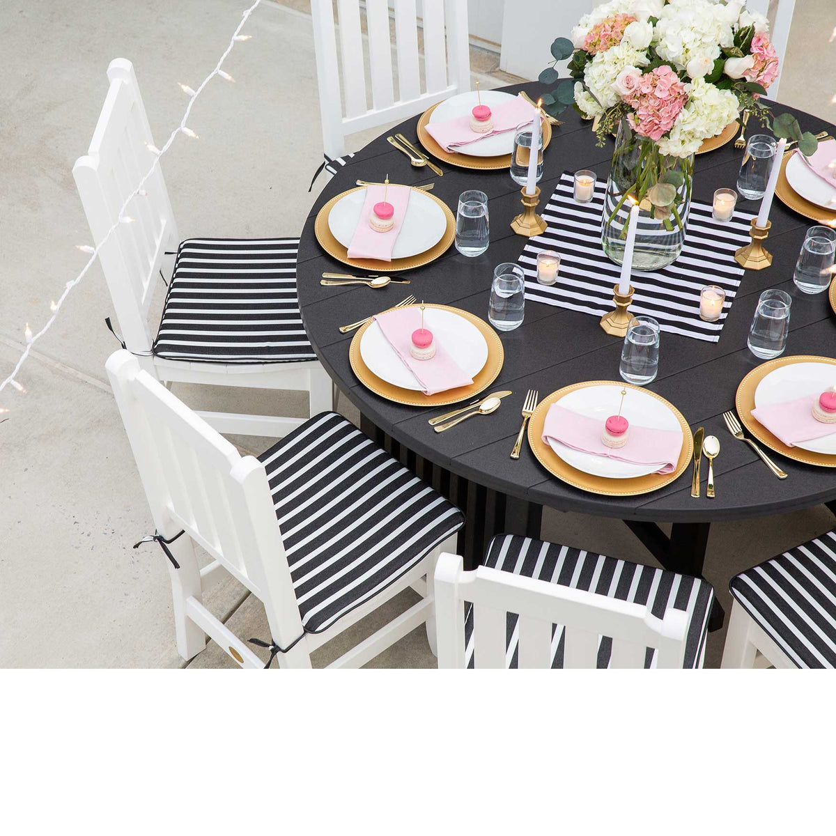 Overhead view of a black round poly dining table set with gold chargers and white slat back chairs