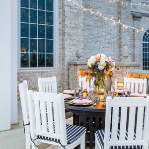 White poly dining chairs with black striped seat cushions around a dark round patio table set with flowers