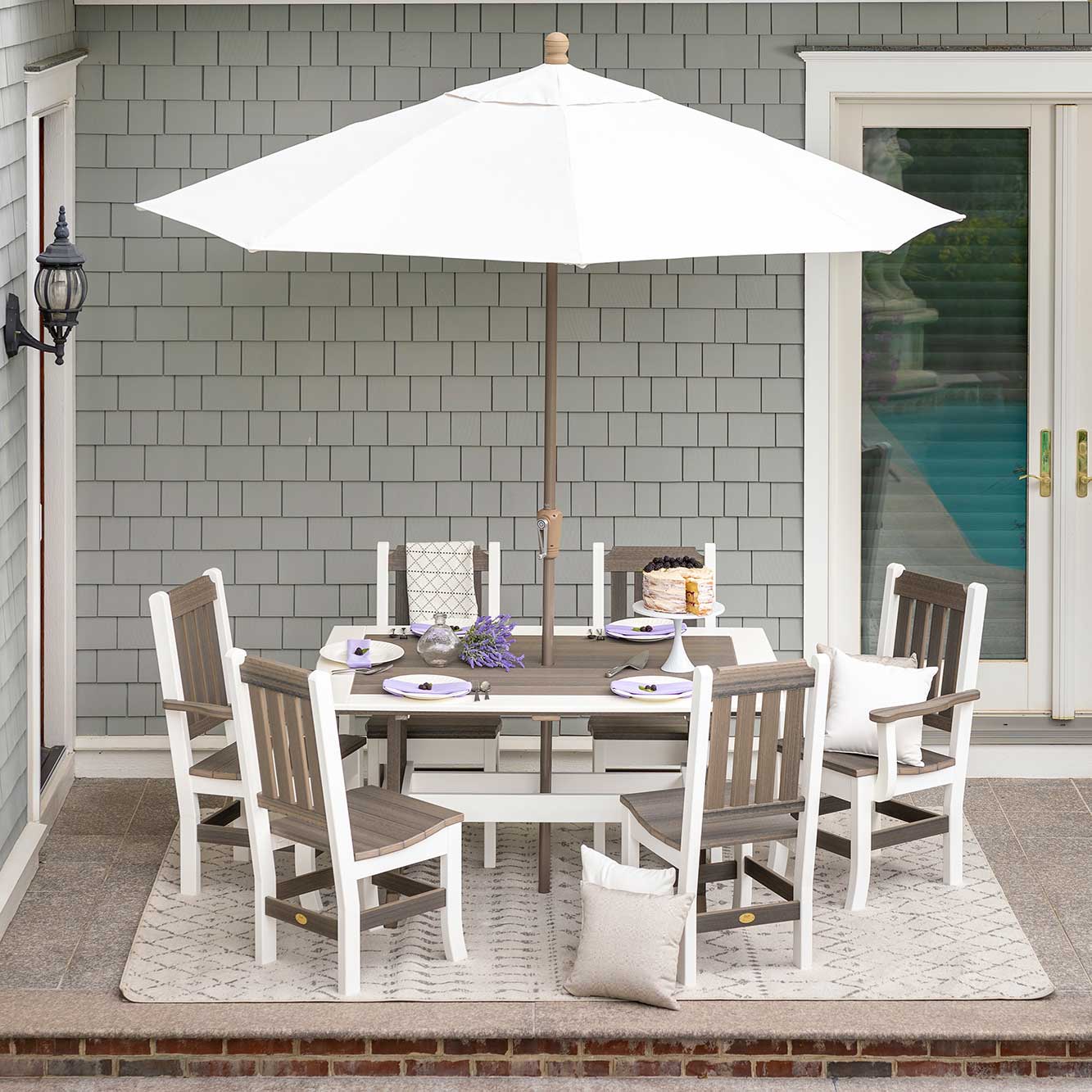 White and driftwood poly rectangular dining table with six slat back chairs under a white market umbrella