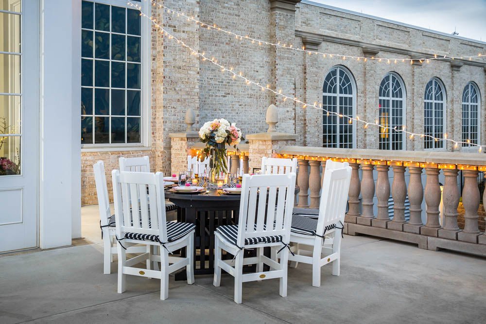 White poly slat back chairs with black striped cushions around a dark round table on a lit stone terrace