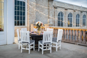 White poly slat back chairs with black striped cushions around a dark round table on a lit stone terrace