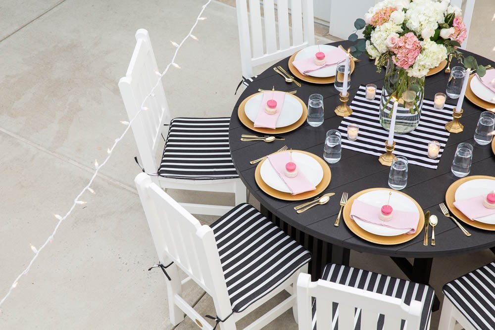 Black round poly patio table set with gold chargers, pink napkins and white striped cushion chairs
