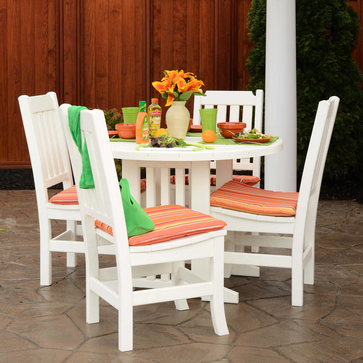 White poly round dining table for four with striped orange cushions and a lunch spread on a patio