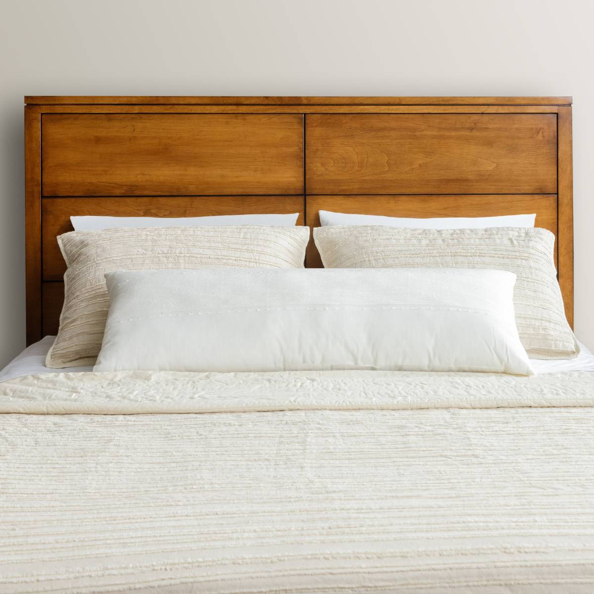 Head-on view of the maple panel headboard with grid-style panels behind cream pillows and a bolster