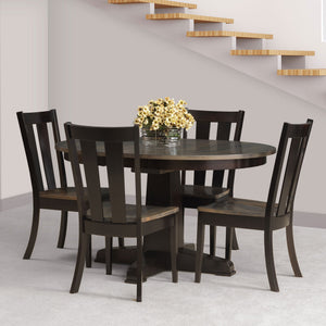 Round pedestal dining table in near black with slat back chairs and a bouquet under an open staircase