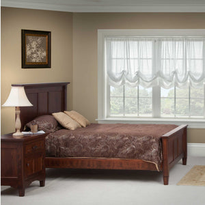 Dark cherry panel bed with nightstand and lamp in a bedroom with brown paisley bedding and sheer curtains