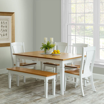 White painted farmhouse dining table with an oak top, four chairs and a matching bench in a bright dining room