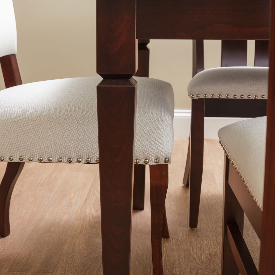 Close-up of the notched table leg in dark cherry with nailhead-trimmed cream chair seats in a dining room