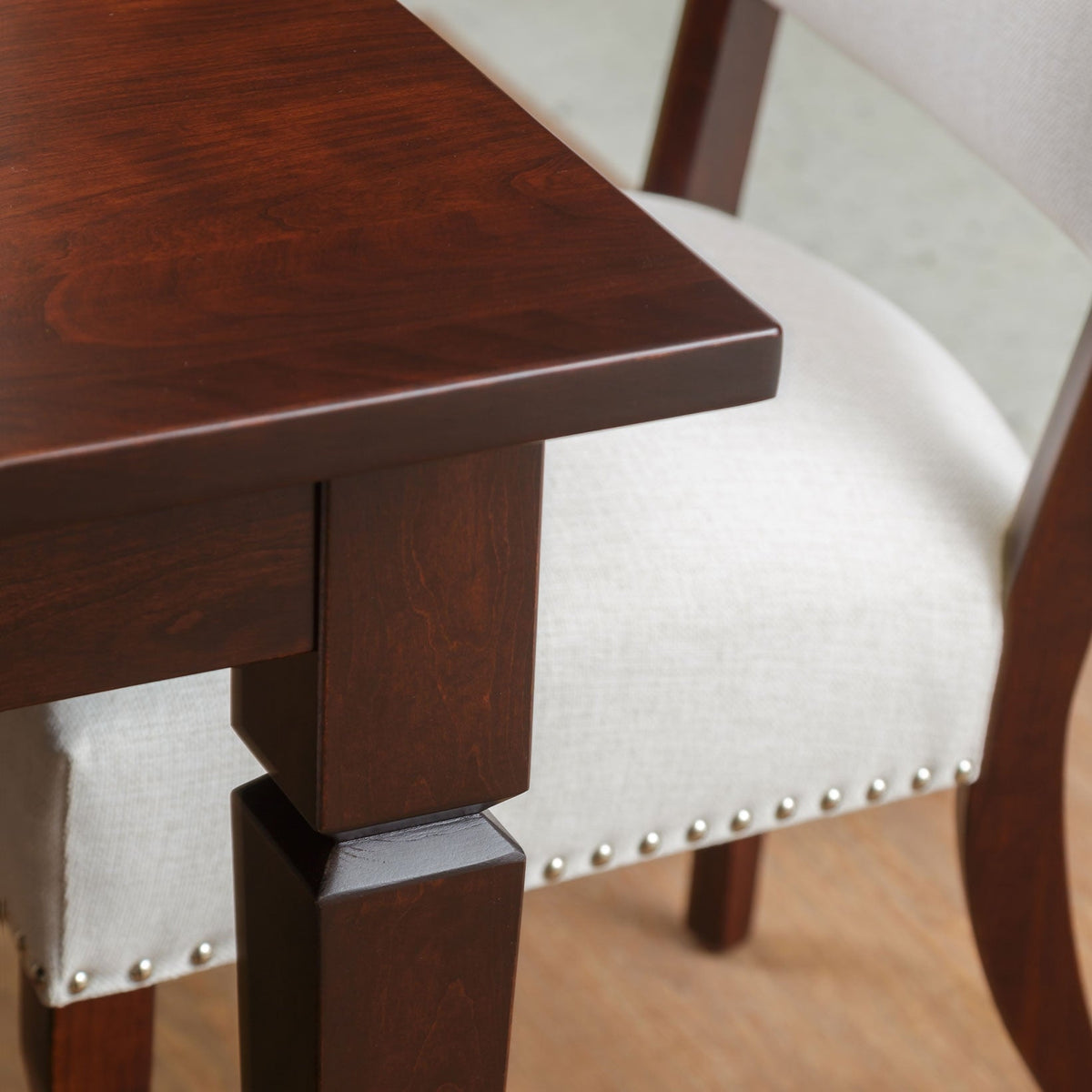 Detail of the dining table's square notched leg and thick cherry top beside an upholstered chair seat