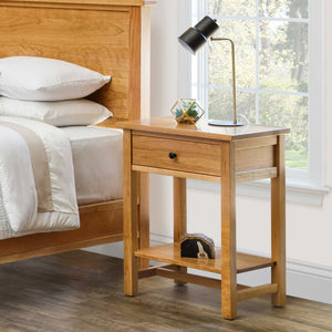 Open one-drawer cherry night table with a lower display shelf beside a bed, holding a lamp and geometric terrarium by a window