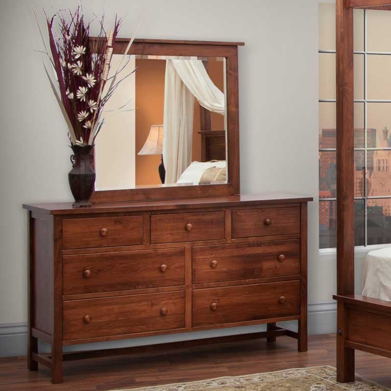 Rich cherry framed dresser mirror above a seven-drawer dresser holding a vase of dried flowers