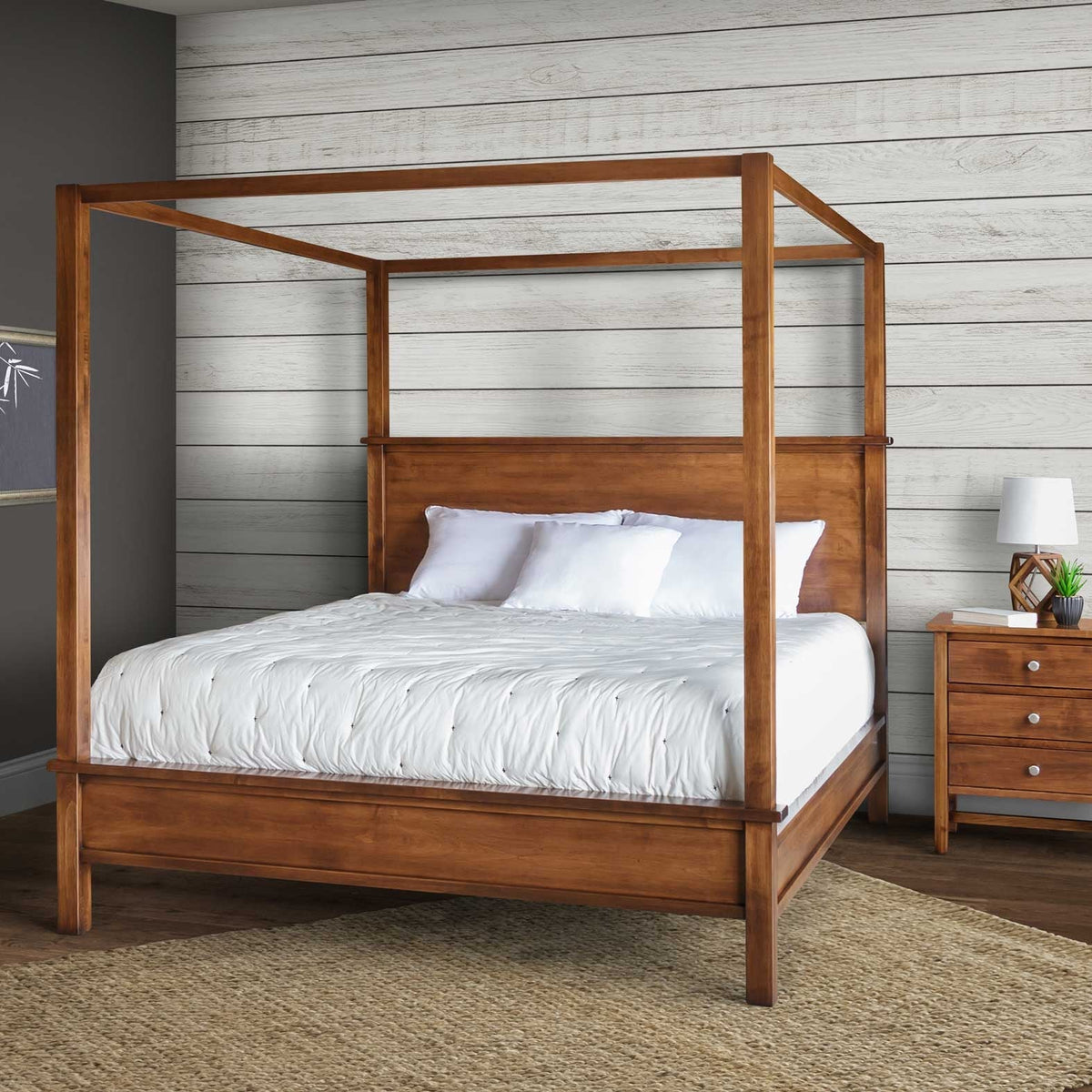Honey brown canopy queen bed with white bedding staged against white shiplap next to a three-drawer nightstand