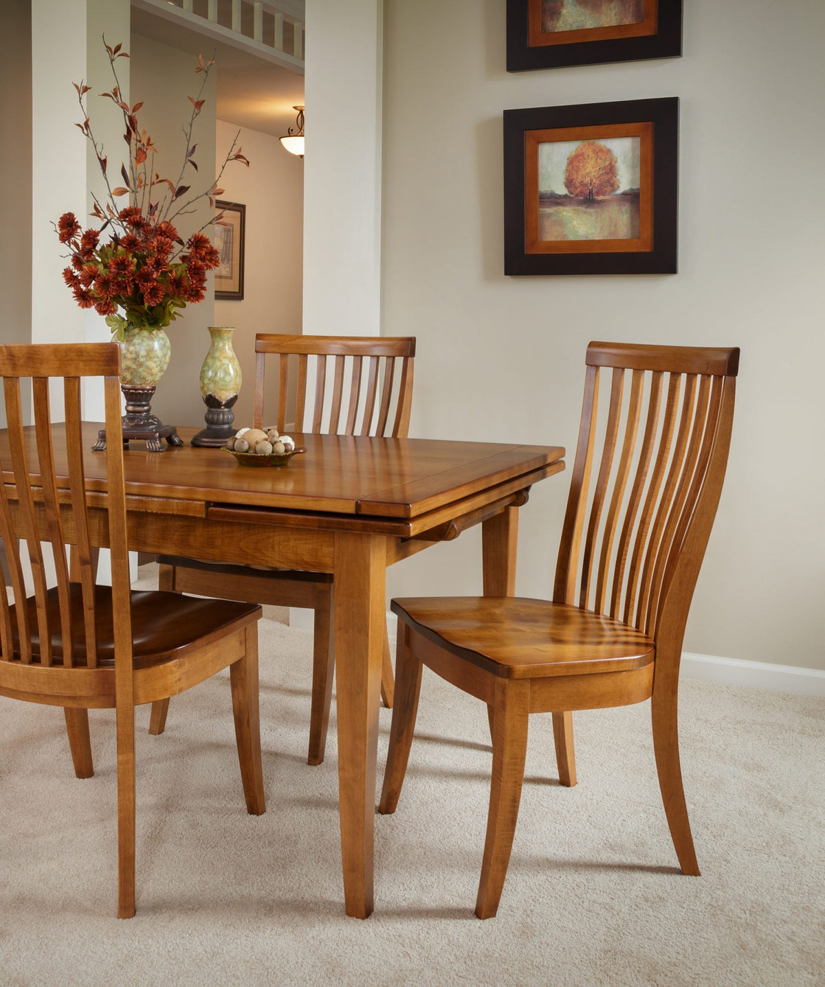 Curved slat back dining chairs in a golden oak finish around an extension leg table in a carpeted dining room