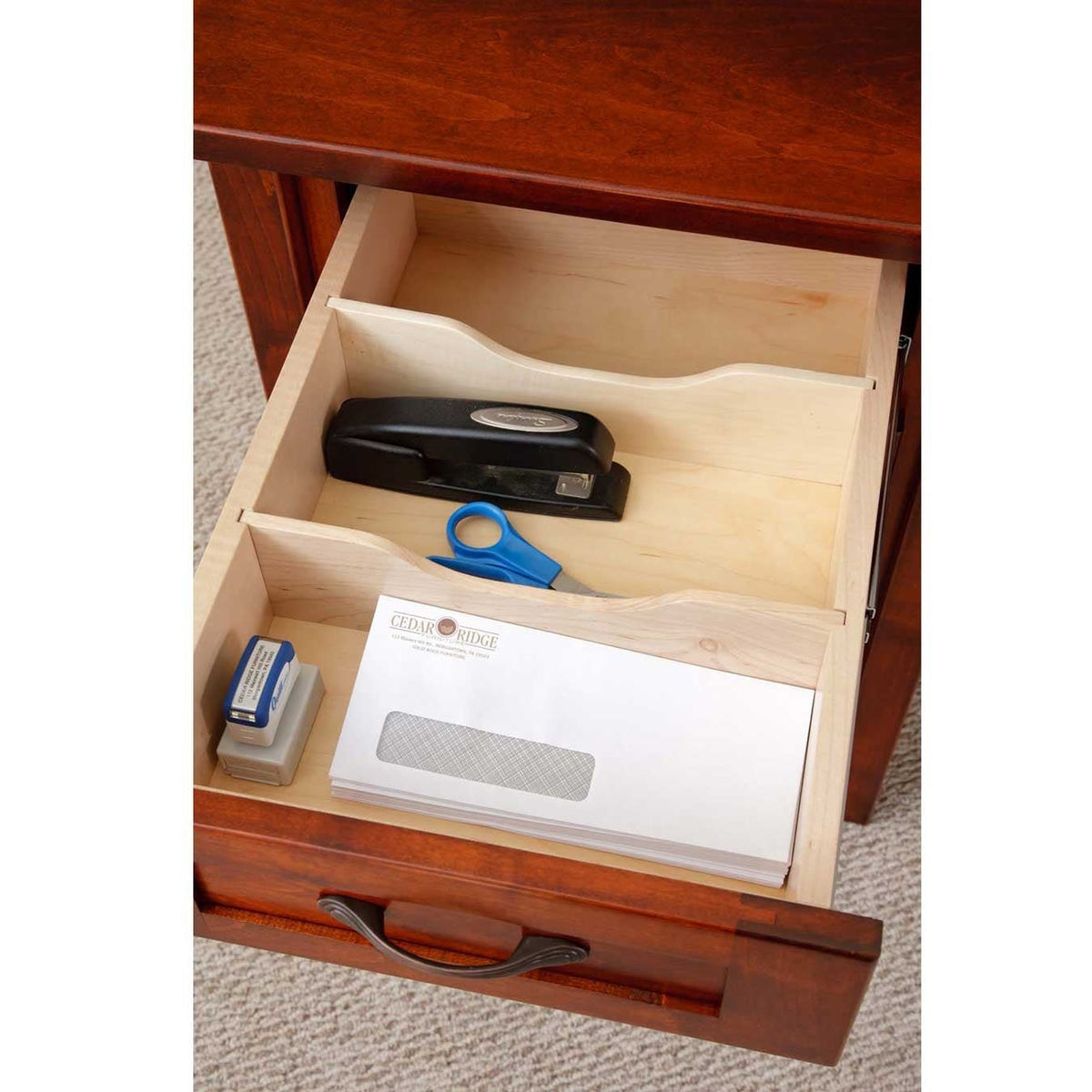 Open desk drawer detail showing maple-lined interior with divided organizer trays holding a stapler and scissors under a cherry top