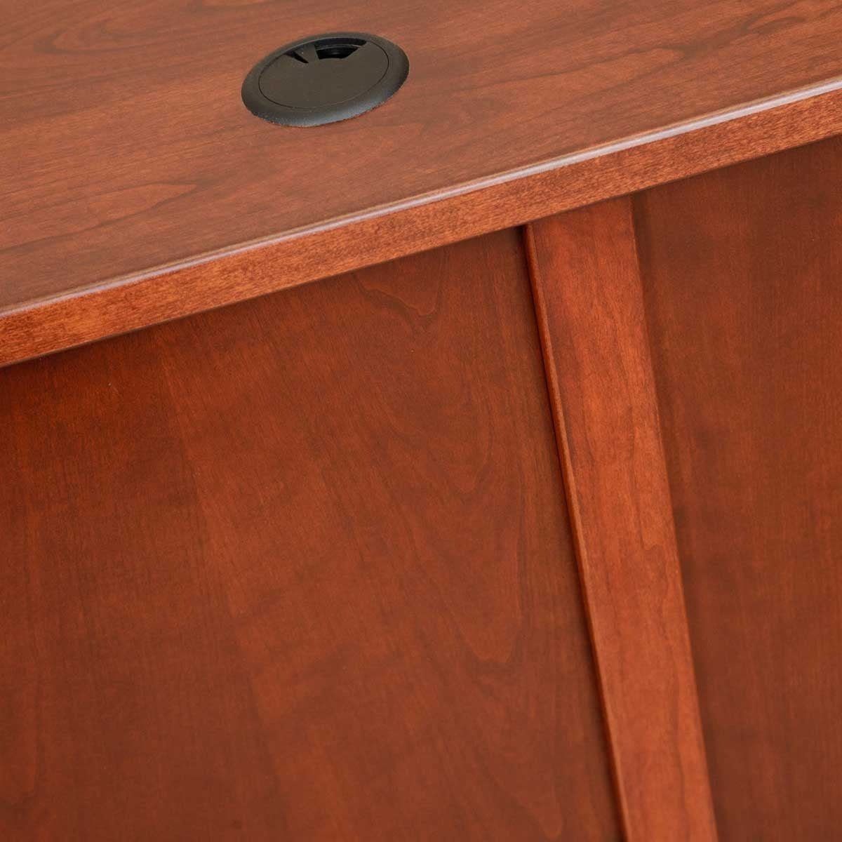 Close view of a warm cherry desktop edge with round black wire grommet and paneled back framing