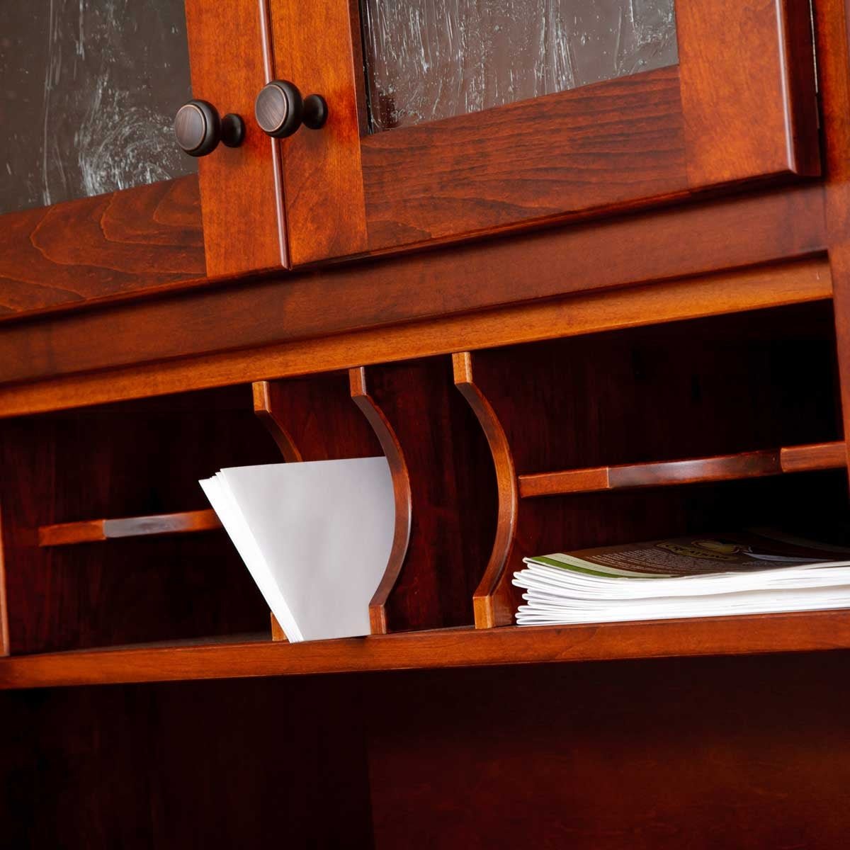 Hutch letter slots with envelopes and papers below glass cabinet doors with dark round knobs in a cherry finish
