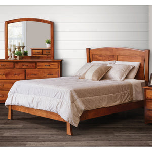 Modern arched panel bed in warm cherry with curved posts and low footboard beside a mirrored dresser