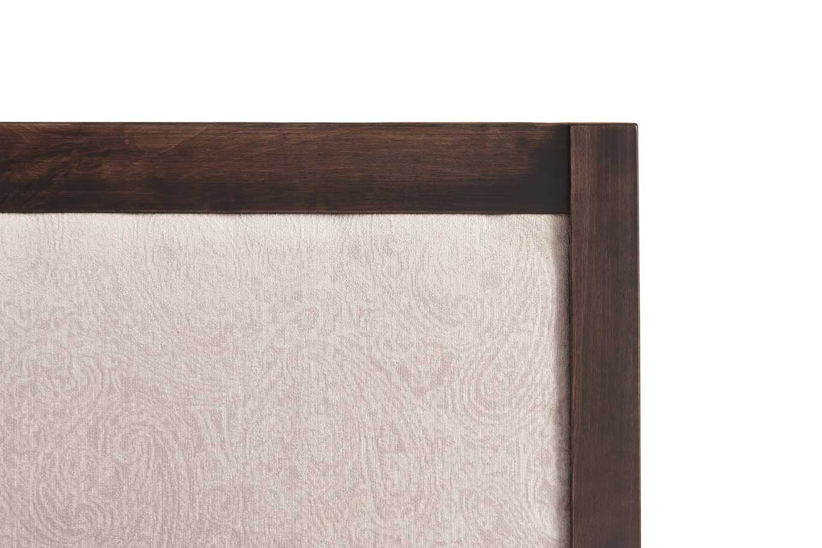 Close-up of the bed's dark wood frame corner around the cream paisley upholstered headboard panel