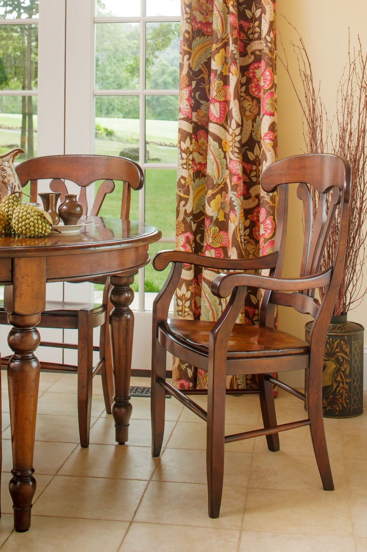 Country style cherry arm chair with a rounded crest rail and wood seat beside a turned leg round dining table