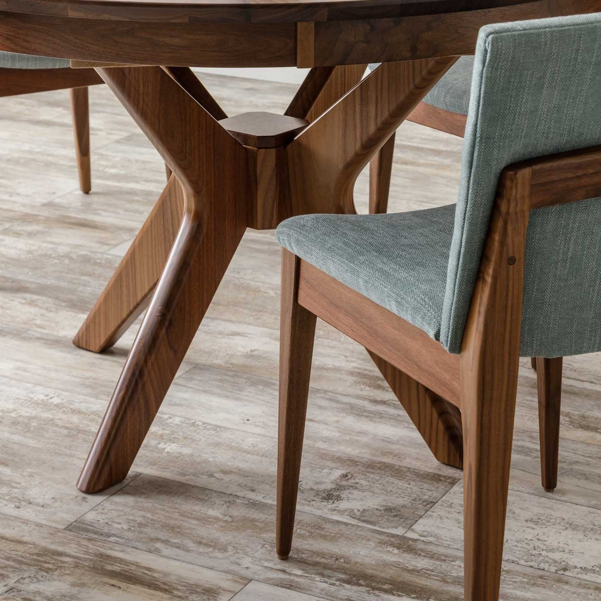 Detail of the round walnut table's crossed sculpted base beside a green fabric mid century chair
