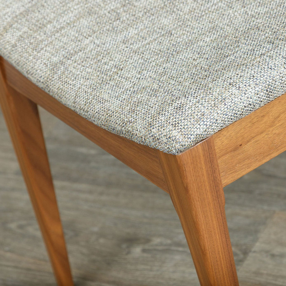 Close-up of a dining chair's woven gray upholstered seat and smooth cherry frame corner