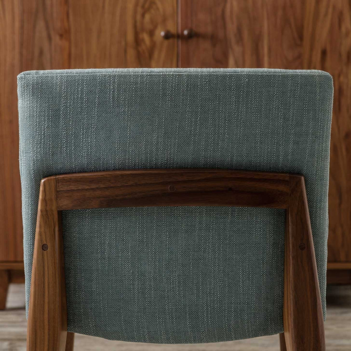 Back view of the upholstered dining chair showing green fabric and a curved walnut back rail