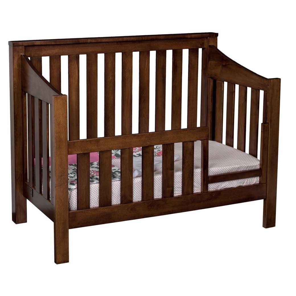 Walnut mission crib converted to a toddler bed with a slatted safety rail and floral bedding