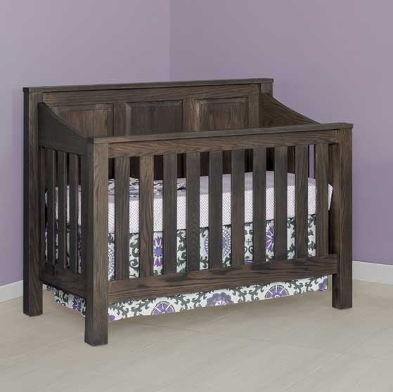 Gray oak convertible crib photographed in a nursery corner with lavender walls and printed skirt