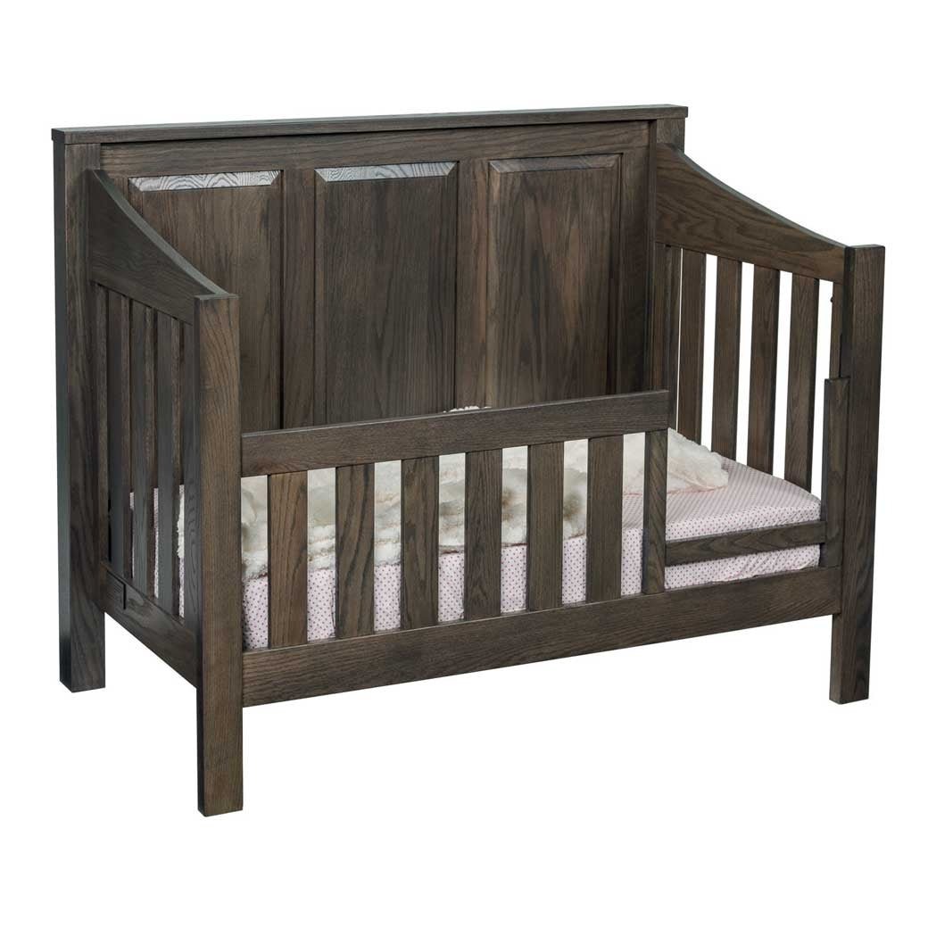 Weathered gray oak crib set up as a toddler bed with a slatted guard rail and panel headboard